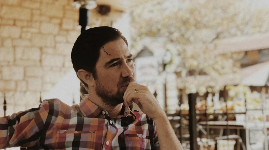 A man sitting outdoors, thoughtful, hand at his chin